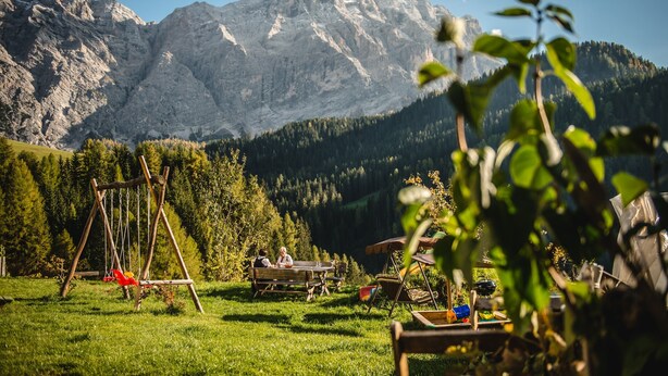 Paisaje montañoso con un columpio y una mesa de picnic en un campo cubierto de césped.
