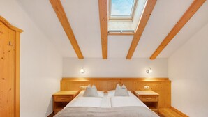 Een slaapkamer met dakraam, houten balken, een bed met kussens, nachtkastjes en een houten garderobe.