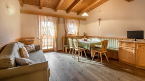 Een gezellige kamer met een houten plafond, een eettafel met stoelen, een bank en een televisie op een houten kast.
