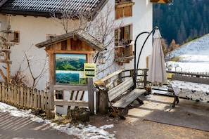 Un bâtiment rustique avec un banc en bois, un panneau indiquant l’arrêt d’un navette de ski, et une vue sur un paysage montagneux.