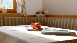 Een kamer met een raam, een potplant, een gestreepte bank en een tafel met appels en een boek.
