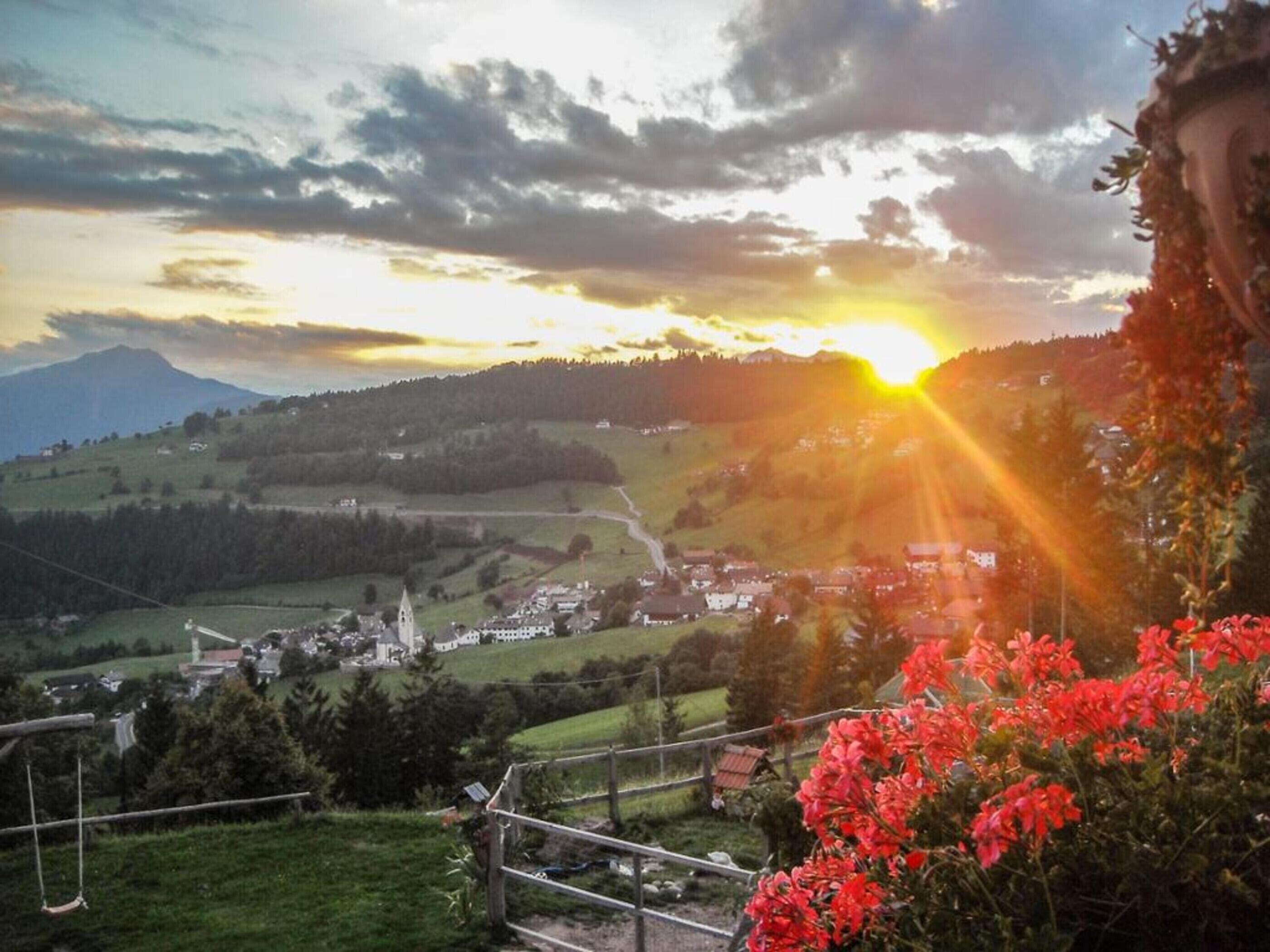 Une vue pittoresque d’une ville avec une église imposante, entourée d’une végétation luxuriante et dominée par des montagnes en arrière-plan.