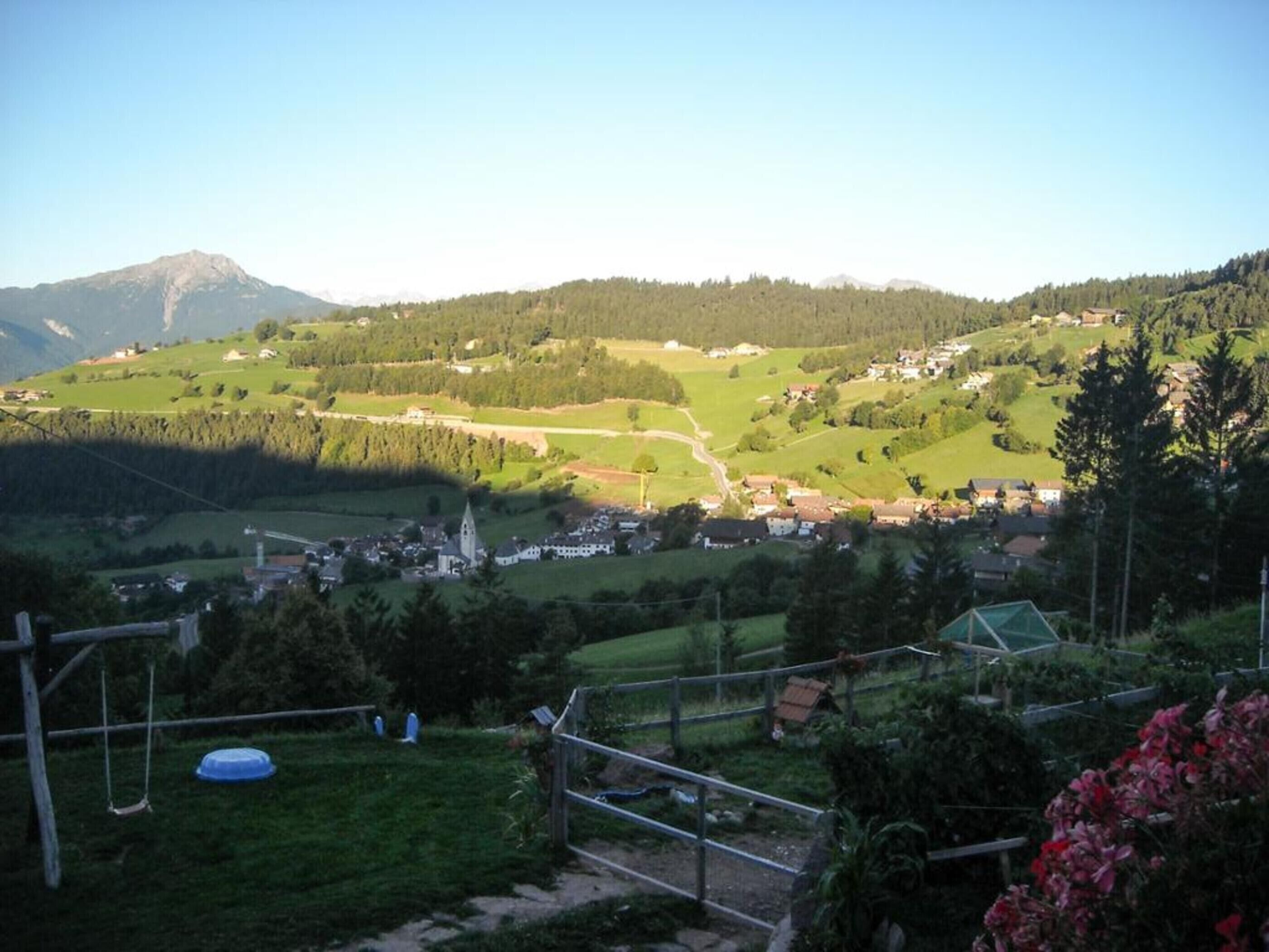 Ländliche Landschaft mit einem Dorf, grünen Feldern und einem Berg im Hintergrund.