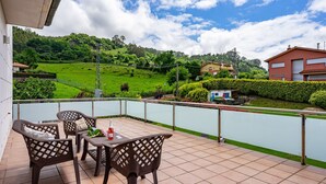 A balcony with outdoor furniture, a view of a green landscape, and a building in the background. - Country House 'Casa La Manzana' with Mountain View, Private Terrace and Wi-Fi (Villaviciosa)