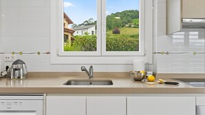 A kitchen with a window view of a house and greenery. - Country House 'Casa La Manzana' with Mountain View, Private Terrace and Wi-Fi (Villaviciosa)