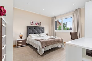 Un dormitorio con cama, mesita de noche, lámpara y ventana con cortinas.