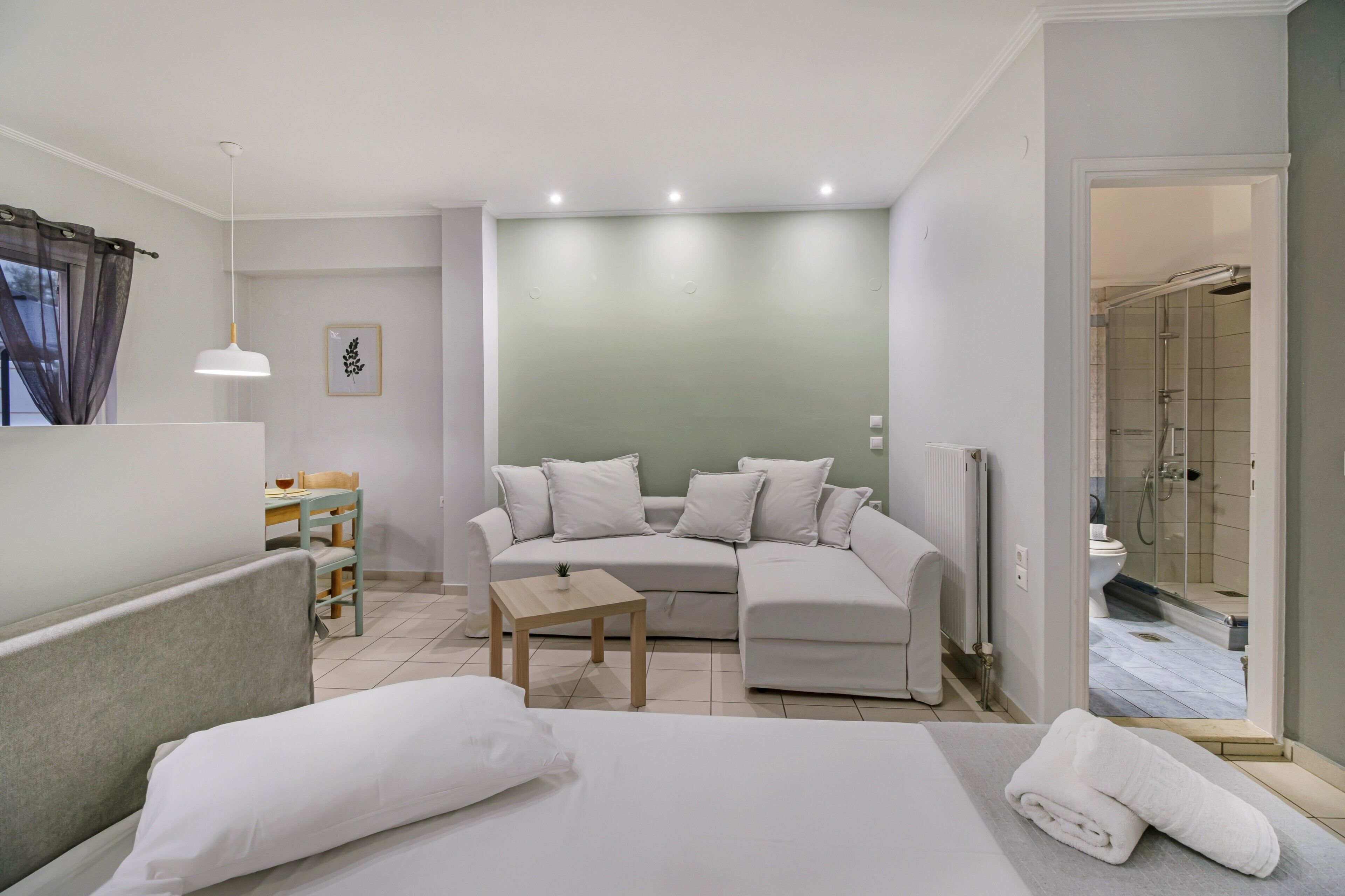 Ein modernes Hotelzimmer mit Bett, Sofa, kleinem Tisch, Sessel und Duschbereich.