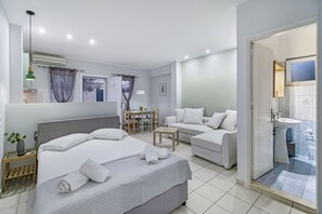 Een hotelkamer met een bed, een slaapbank, een klein tafeltje en een badkamer met wastafel en spiegel.