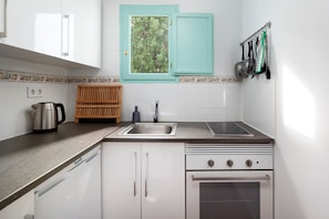 A kitchen with white cabinets, a double sink, a stove, and a window with a view of trees.