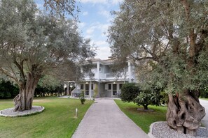 A building with a central courtyard, surrounded by trees and a gravel path leading to the entrance.