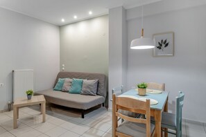 A modern living room with a sofa, a dining table with chairs, a hanging light fixture, and a framed picture on the wall.