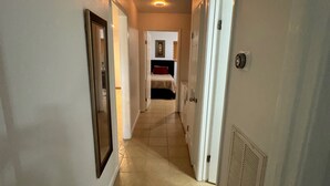 Um corredor estreito com paredes brancas, piso ladrilhado e portas que dão para quartos.