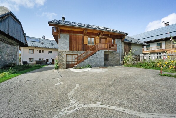 A stone building with a wooden staircase leading to a balcony, surrounded by a paved area and other buildings.