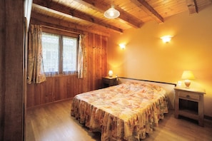 A bedroom with wooden walls, a bed with a floral bedspread, two bedside lamps, and a window with curtains.