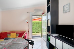 A room with a bed, a TV, a sofa, and a door leading to a balcony.