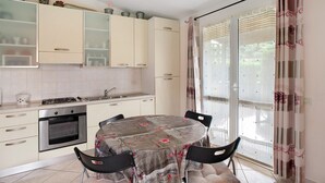 A kitchen with a dining table, cabinets, and a window with curtains. - Villa 'Pairola' with Sea View, Private Garden and Air Conditioning (San Bartolomeo al Mare)