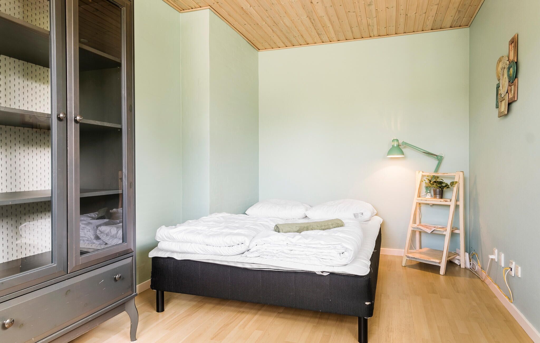 Une chambre à coucher comprenant un lit, une armoire, une table de chevet, une lampe et une petite étagère avec une plante.