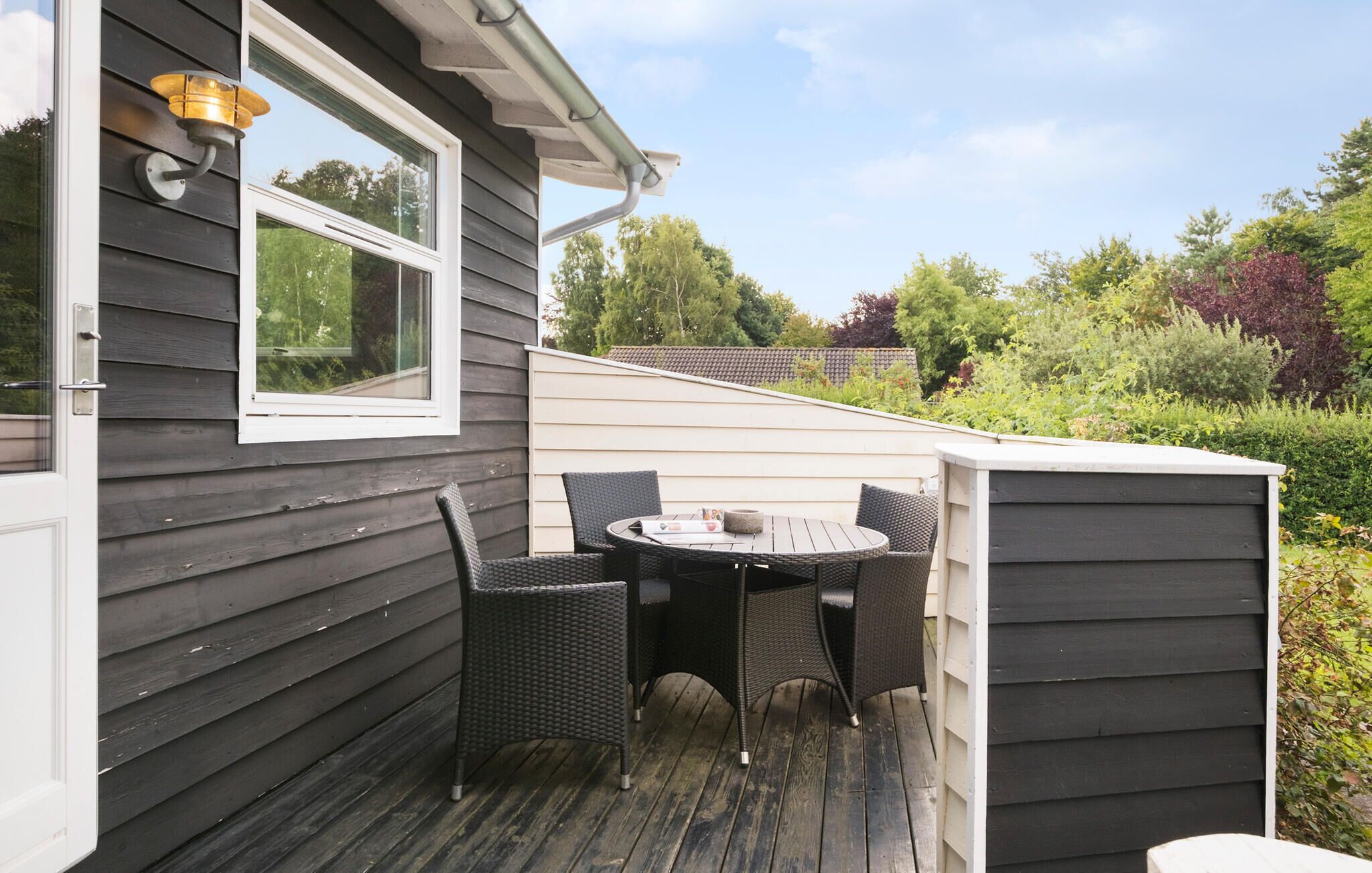 Een klein terras buiten met een tafel, stoelen, een raam en een lamp.