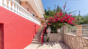 Un edificio rosso con una scala in pietra che conduce a un balcone bianco, circondato da vegetazione e un cielo sereno.