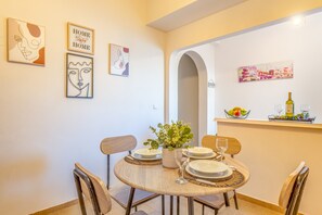 A dining area with a round table, chairs, plates, a vase with flowers, and wall art. - Apartment 'Maestro' with Shared Terrace, Wi-Fi and Air Conditioning (Paxos)