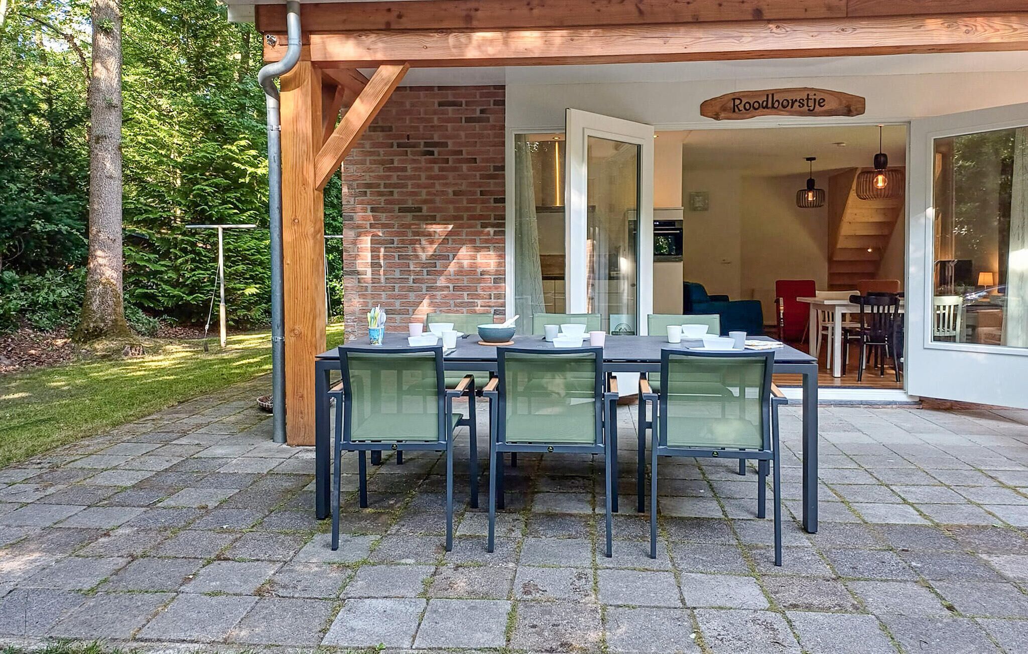 Ein Essbereich im Freien mit einer Backsteinmauer, einer Holz-Pergola und einem Schild mit der Aufschrift 'Roodborstje'.