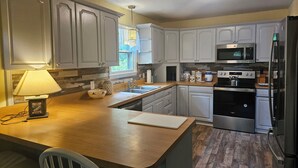 A kitchen with white cabinets, a wooden countertop, a sink, a stove, and a microwave. - YEAR'ROUND FAMILY FUN! (Warrensburg)