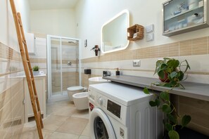 A modern bathroom with a shower, toilet, and washing machine, a wooden ladder, and a potted plant. - Non dire Gatto – Elegant Rooftop Apartment in Alghero (Alghero)