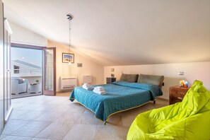 A bedroom with a bed, a bright green bean bag, a bedside table with a lamp, and a view of the outside balcony. - Non dire Gatto – Elegant Rooftop Apartment in Alghero (Alghero)