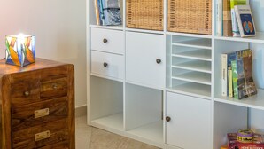 Ein weißes Regal mit Büchern, Korbwannen und einem Holztischchen mit einer dekorativen Lampe.
