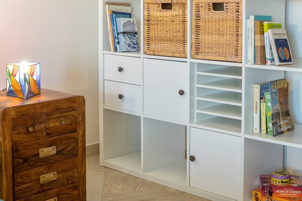 Una estantería blanca con libros, cestas de mimbre y una mesita de madera con una lámpara decorativa.
