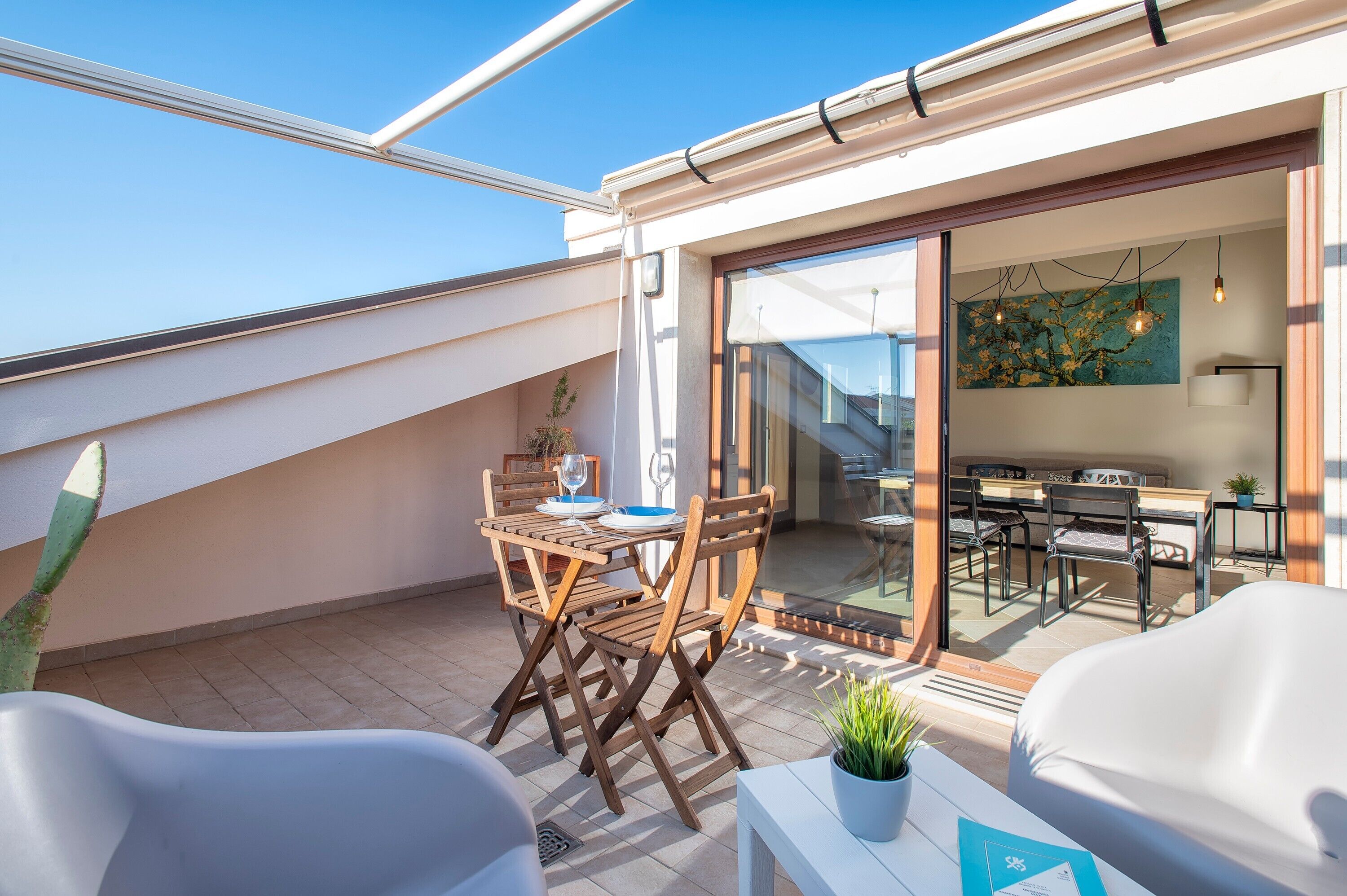 A rooftop terrace with a dining table, chairs, and a potted plant.