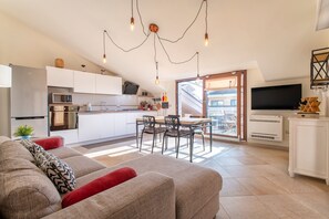 A modern kitchen with a dining area, a flat-screen TV, and a large window. - Non dire Gatto – Elegant Rooftop Apartment in Alghero (Alghero)