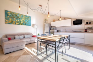 A modern kitchen with white cabinets, a wooden dining table, and a flat-screen TV mounted above.