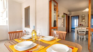 A dining area with a wooden table set for four, yellow placemats, white plates, and wine glasses. - Apartment 'Terrace with Sea View and Barbecue' with Sea View, Wi-Fi and Air Conditioning (Alghero)