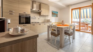 A modern kitchen with wooden cabinets, a built-in oven, and a dining area with a table and chairs. - Apartment 'Terrace with Sea View and Barbecue' with Sea View, Wi-Fi and Air Conditioning (Alghero)