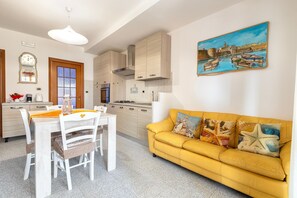 A modern kitchen with wooden cabinets, a dining area with a white table and chairs, and a yellow sofa with decorative pillows.
