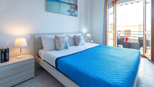 A bedroom with a bed, nightstands, a painting, and a balcony with outdoor furniture. - Apartment 'Terrace with Sea View and Barbecue' with Sea View, Wi-Fi and Air Conditioning (Alghero)