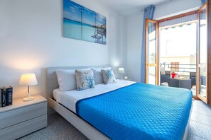 A bedroom with a bed, nightstands, a painting, and a balcony with outdoor furniture.
