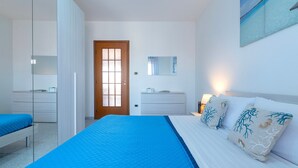 A bedroom with a bed, a wardrobe, a dresser, a mirror, and a door. - Apartment 'Terrace with Sea View and Barbecue' with Sea View, Wi-Fi and Air Conditioning (Alghero)