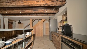 Une cuisine avec des poutres en bois, un réfrigérateur et des étagères remplies d’assiettes et de verres.
