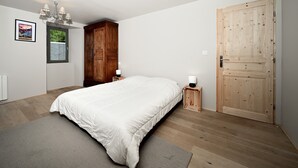 Une chambre à coucher avec un grand lit, une armoire en bois, une porte et une petite table de chevet avec une lampe.