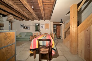 Un comedor con una mesa y sillas de madera, un sofá verde y un techo rústico.