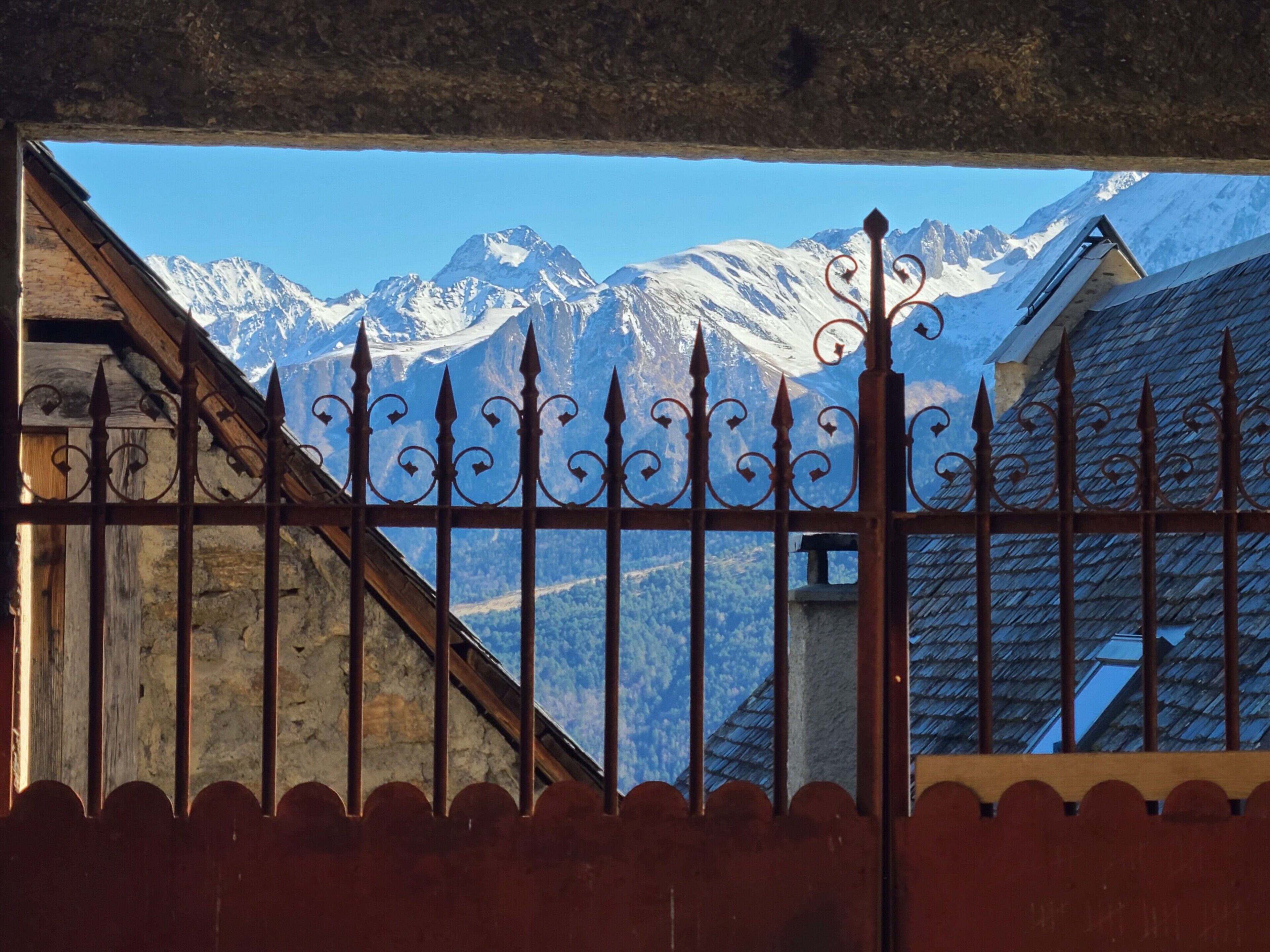 A mountain view through a metal fence with a wooden building in the foreground.