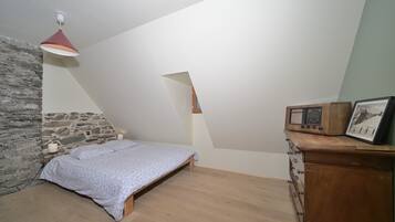 A bedroom with a sloped ceiling, a bed, a dresser, and a stone wall.