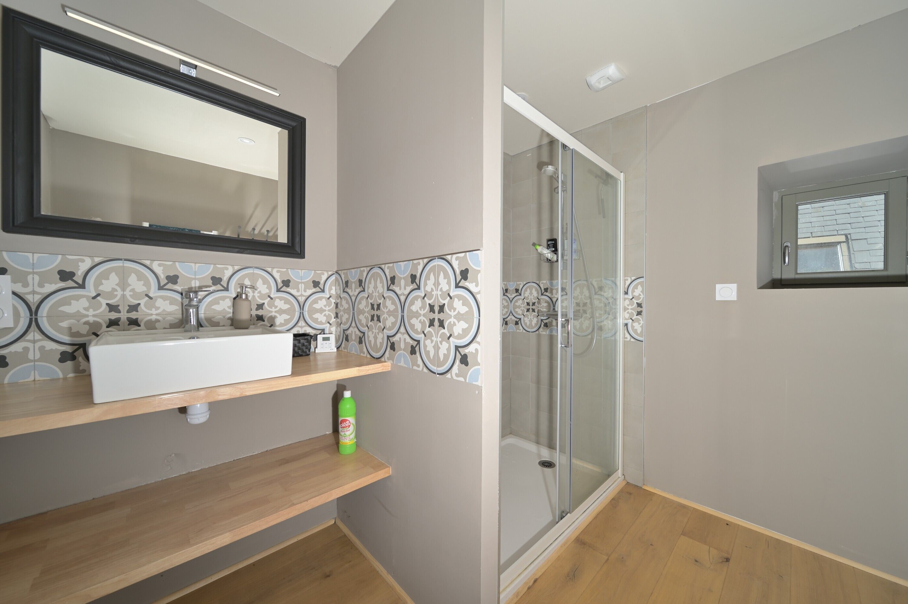 Een badkamer met een spiegel, wastafel, douche en decoratieve tegels.