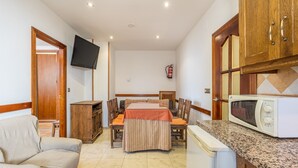 Un espacio habitable compacto con comedor, sofá, televisor montado en la pared y microondas en la encimera.
