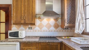 Una cocina con armarios de madera, microondas, estufa y ventana con cortina.