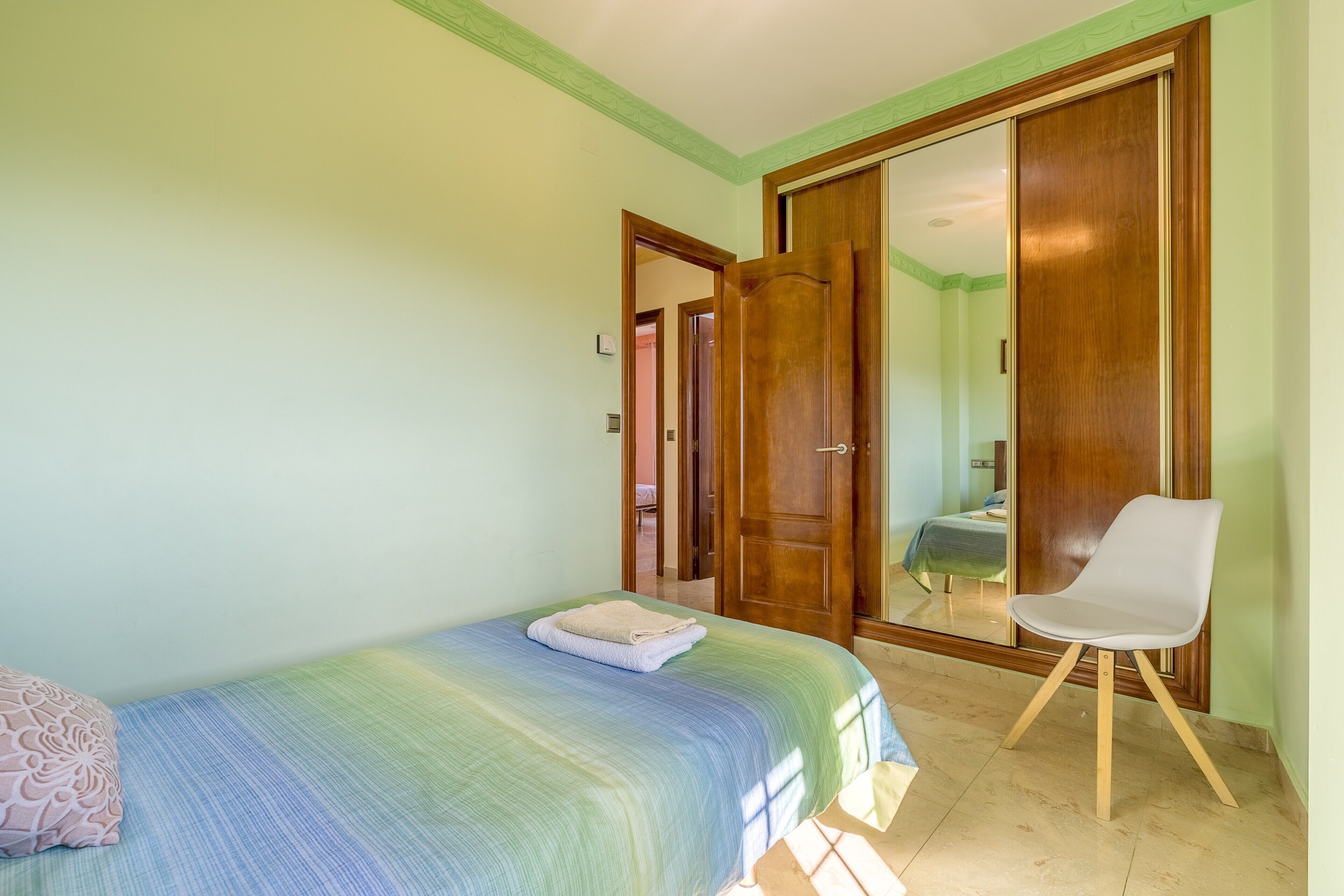 Un dormitorio con cama, una silla y un armario.