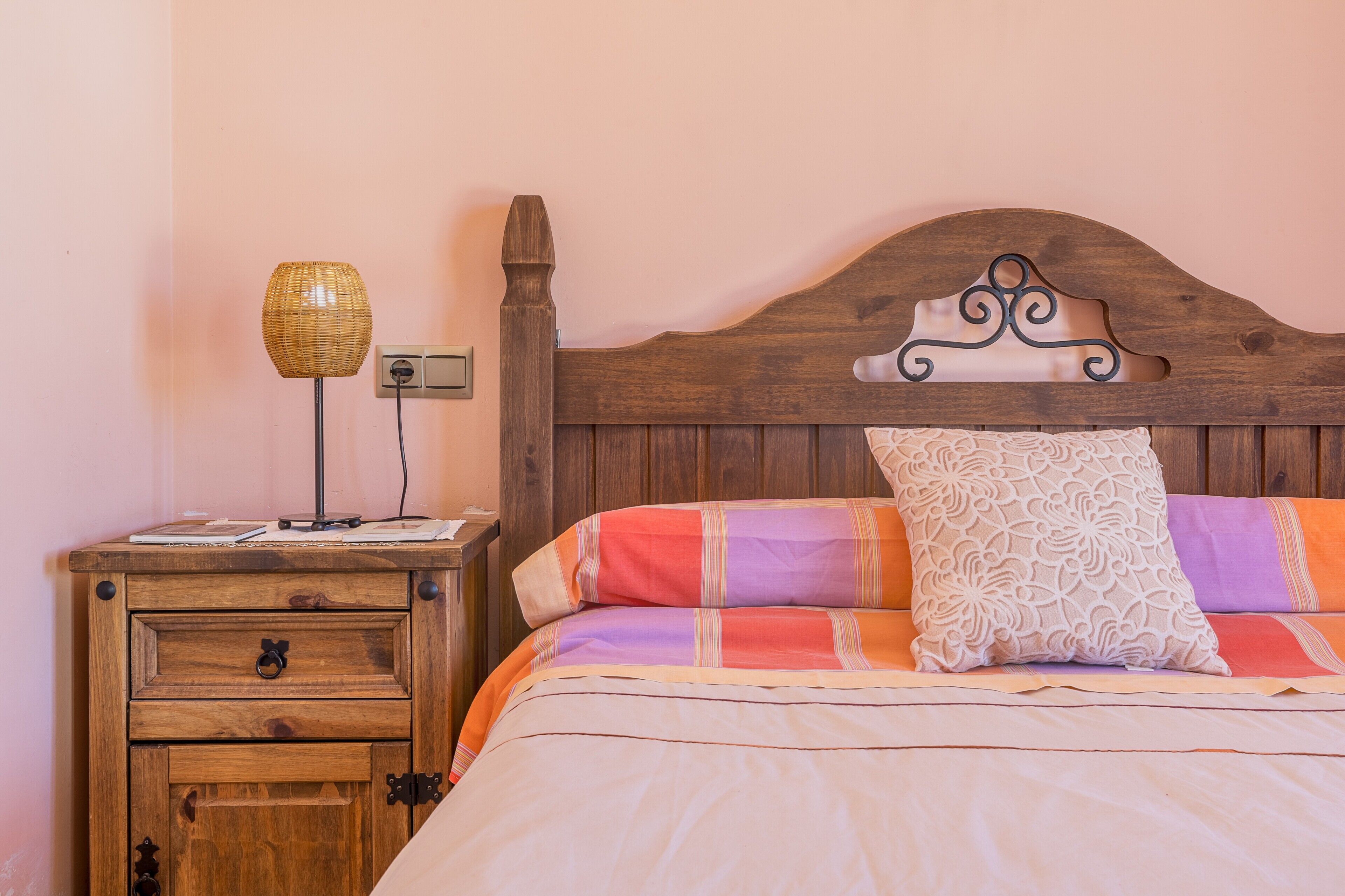 Une chambre à coucher avec une tête de lit en bois, une table de chevet avec une lampe et un lit recouvert d’une literie à motifs.