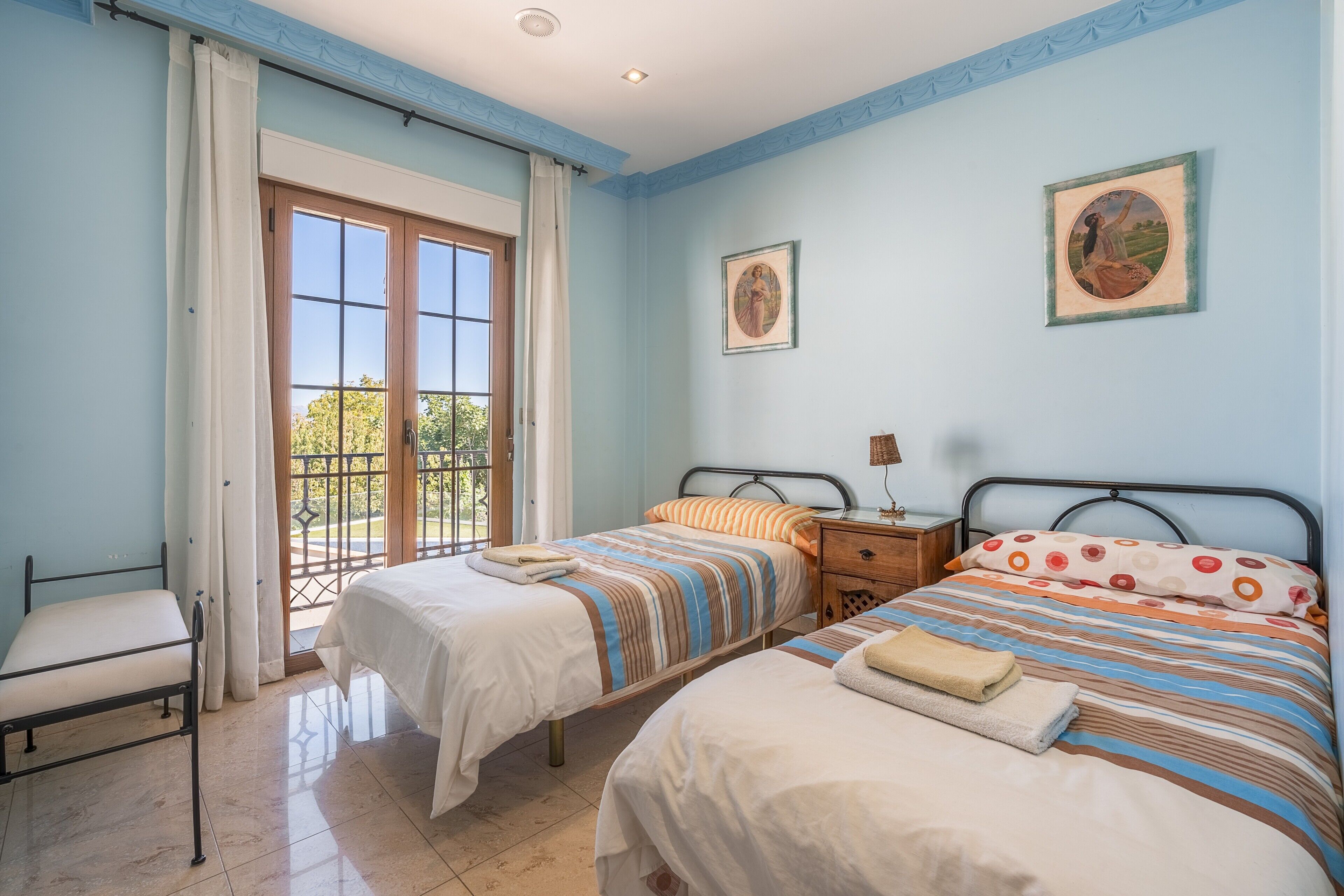 Un dormitorio con dos camas, una mesita de noche, una silla y una ventana con cortinas.